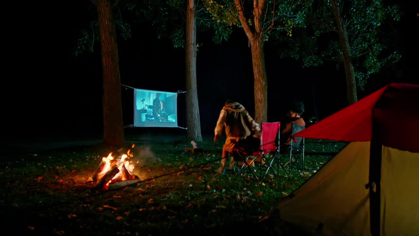 Two boys at a campsite watching a movie on a makeshift screen in the tree