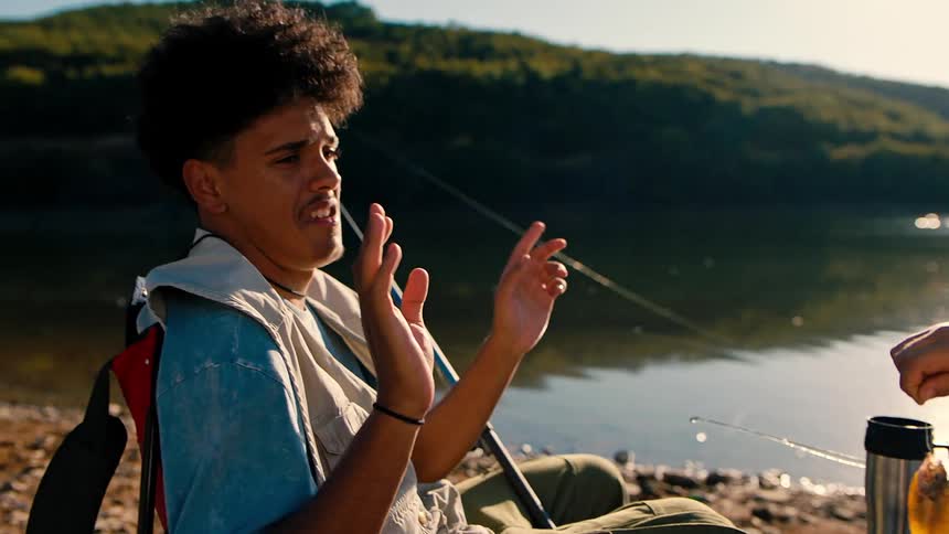 Two brothers on a lake shore laugh about a small fish one of them caught
