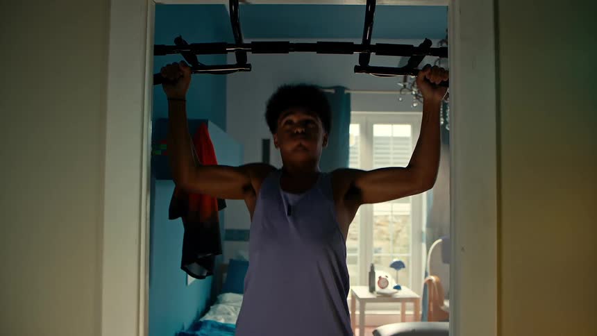 Teenager doing pull ups on a machine on top of a door in a room of the house