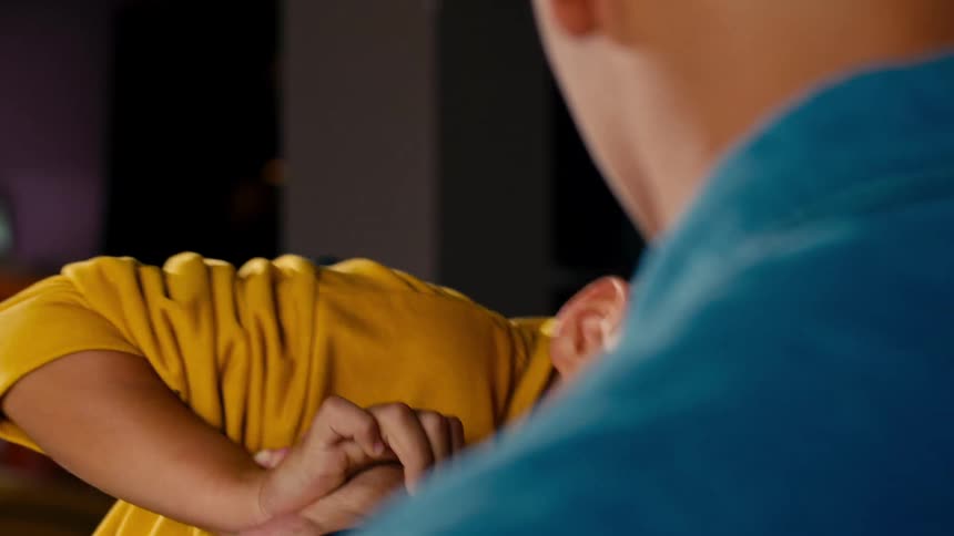 A young boy attempts to arm wrestle his older brother and gets angry when he loses