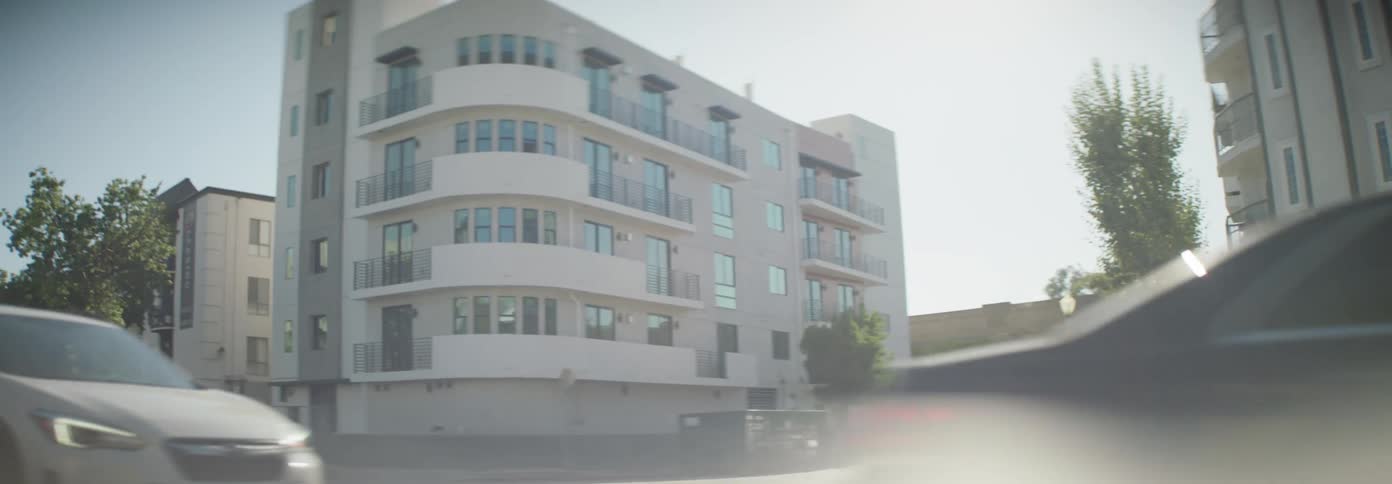 A moving vehicle captures the street view of buildings and parked cars