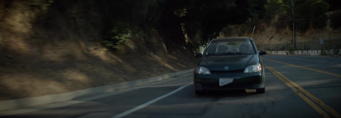 Cars drive alongside a cliff near a tunnel on a sunny day