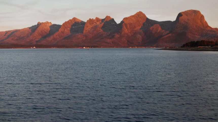 A mountain range bathed in the warm light of sunset reflected in the calm waters below