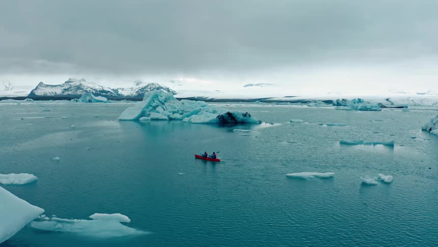 Two people rowing a red boat in the middle of the arctic ocean