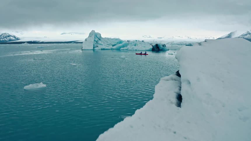 Two kayakers paddle through a serene glacial lagoon