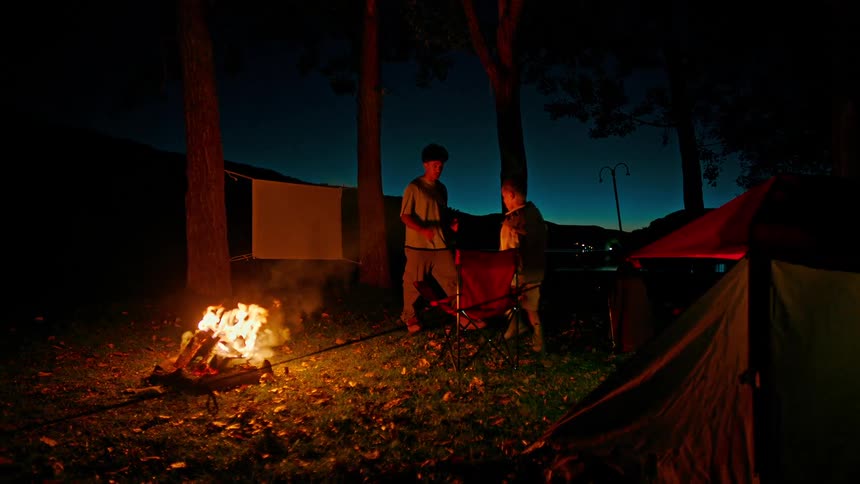Two boys at a campsite at night with a campfire burning