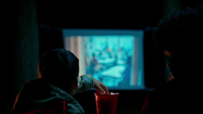 Two people eat popcorn and watch television