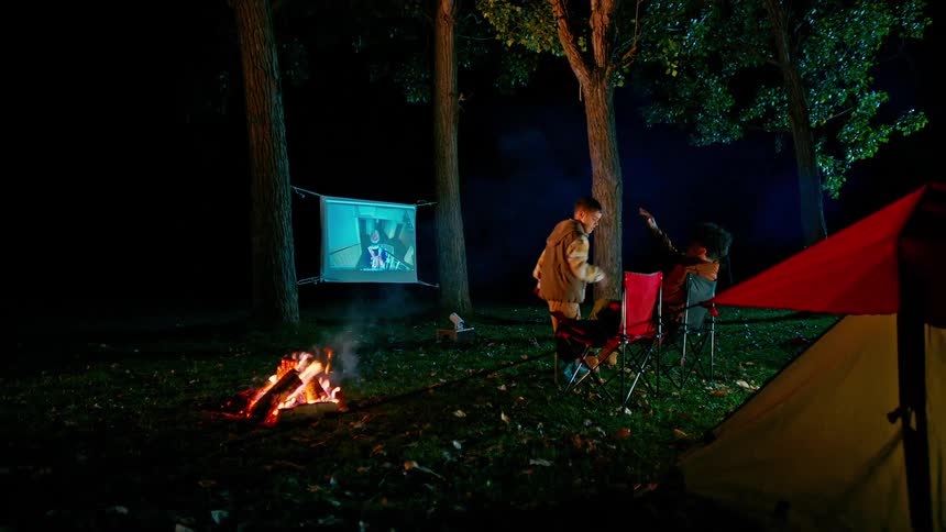 A young boy high fives his brother after adjusting a television set outdoors at a campsite