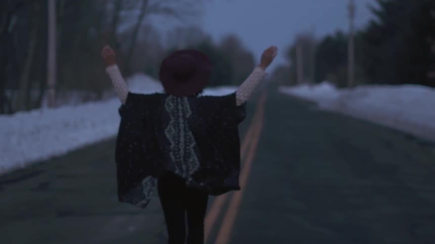 A woman in a hat runs down the middle of a street in winter