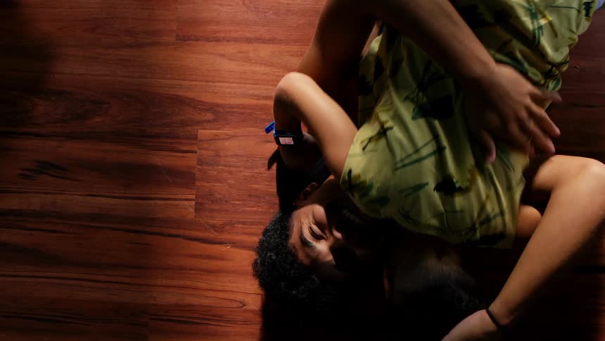 A young boy rolls over and hugs his older brother as both lie on a wooden floor laughing