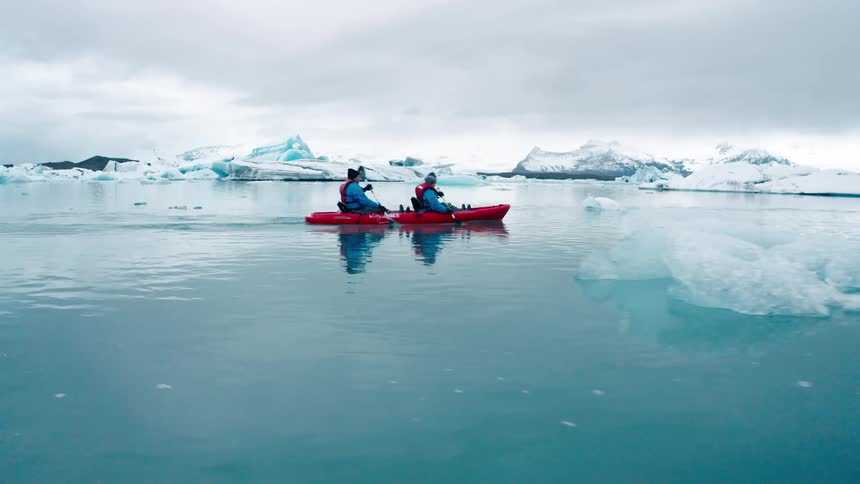 Two people rowing a boat while in an arctic sea with glaciers