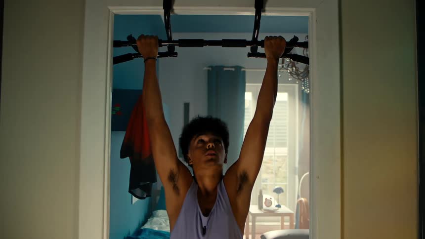 Boy doing pull ups on a piece of equipment attached to the door of a room in the house