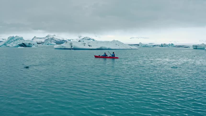 Two people in an orange boat rowing past glaciers