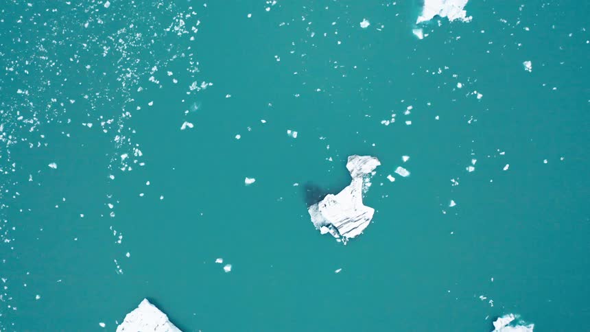 Icebergs and smaller sea ice float on blue arctic waters during the day