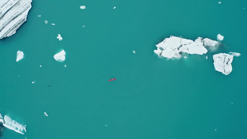 A red kayak floats in teal colored water dotted with chunks of ice