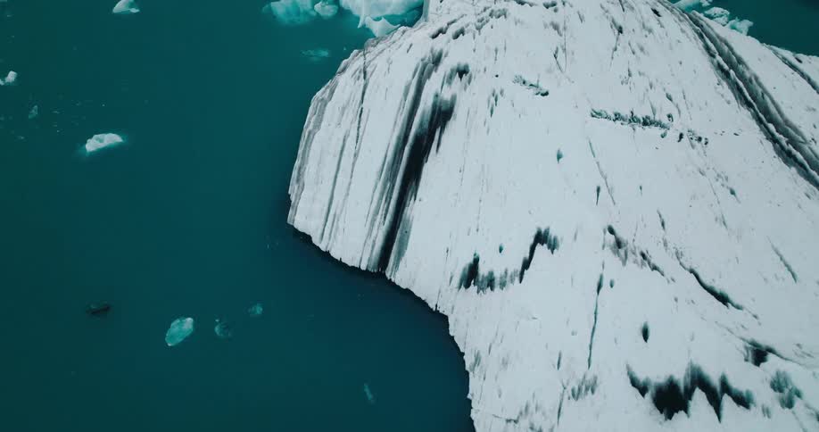 A large coast covered in melting ice as small icebergs float in the ocean nearby