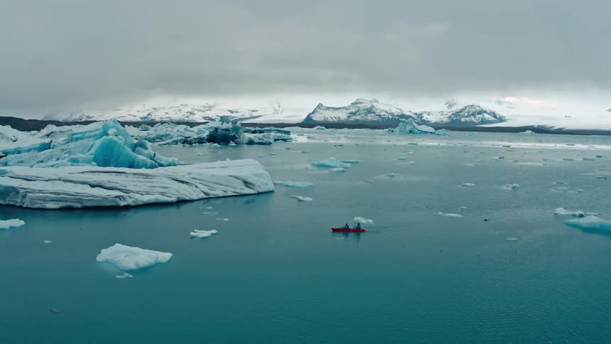 Two people are canoeing through an arctic body of water on a cloudy day