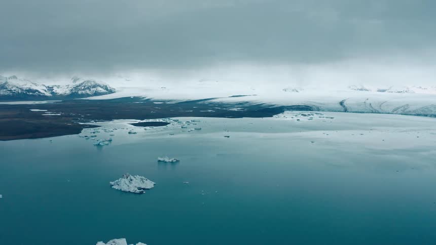 Sea ice floats off an ice covered shore under an overcast sky