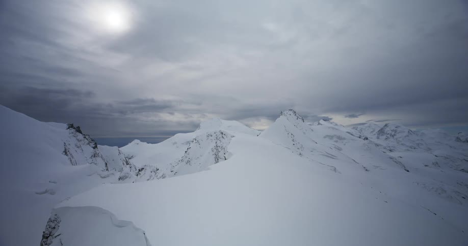 A snowcapped mountain peak with a misty sky and distant glaciers