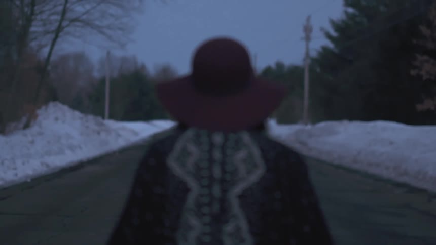 Woman in red hat stands in the center of a snow-lined road