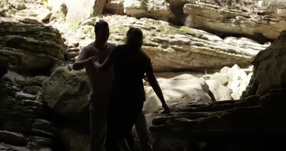 Man helping a woman jump a small gap between some rocks