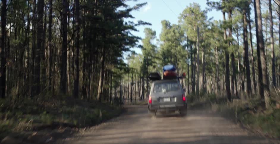 A vehicle drives through a forest with kayaks strapped to the roof