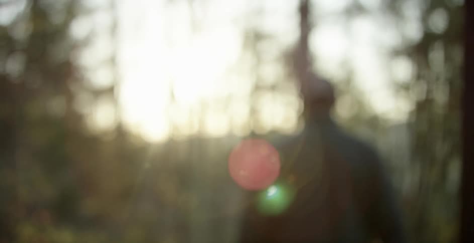 A man and woman walk through a forested area as the sun shines through the trees