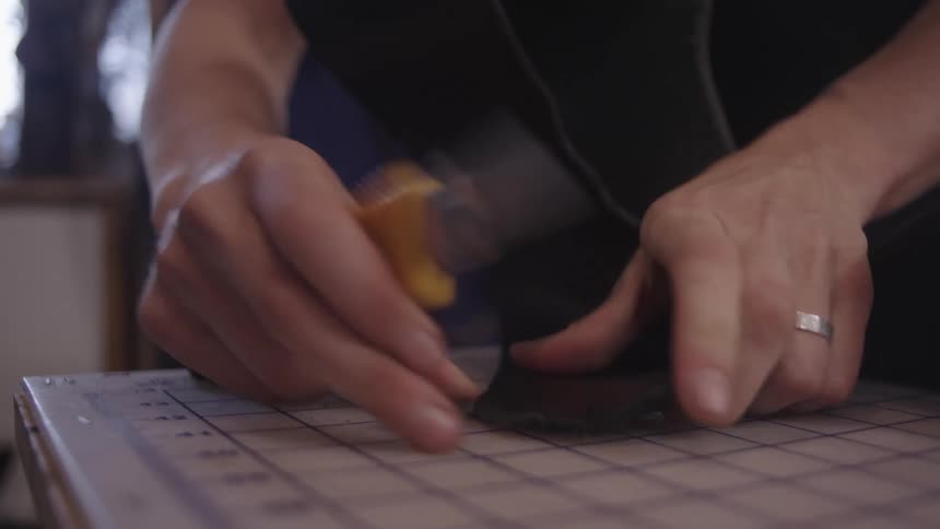 A person cuts black fabric with a blade