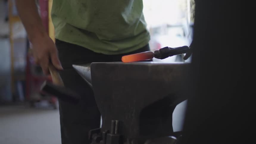 Arms of a person forging a heated metal on top of a surface