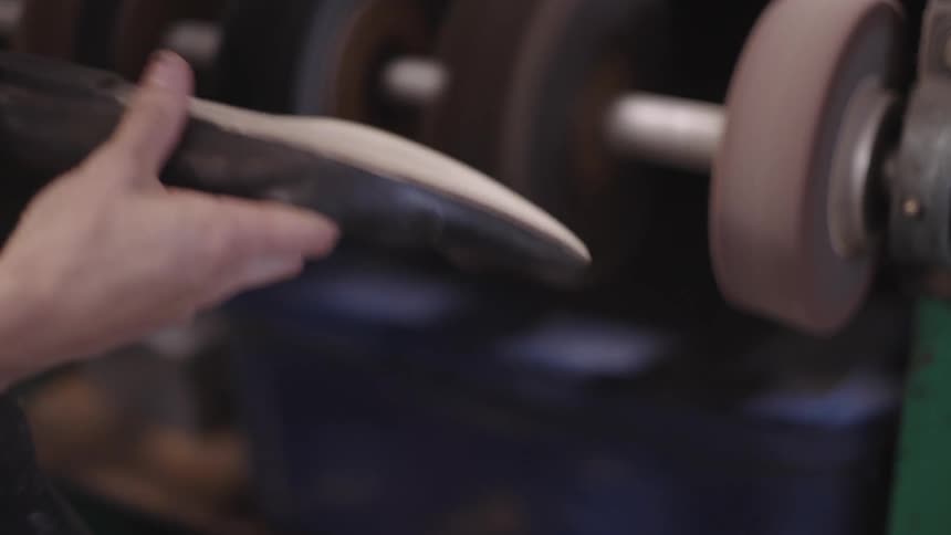 An employee uses a machine to sand off a part of a shoe sole
