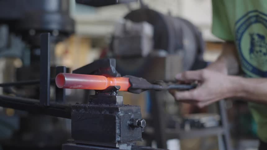 A blacksmith shapes a glowing piece of metal using a pair of tongs