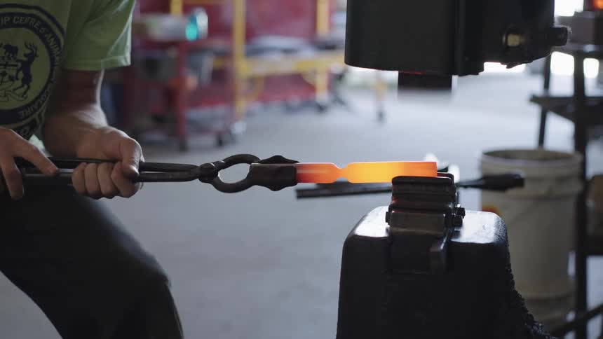 Blacksmith shapes a piece of hot metal on an anvil with a hammer