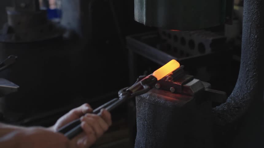 Blacksmith holding a hot metal with a tool and putting it into a machine