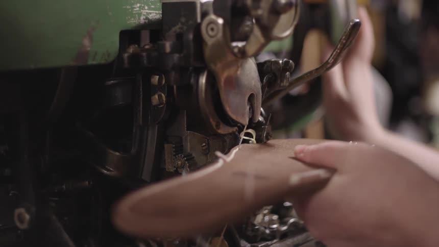 A craftsman uses a sewing machine to stitch leather together