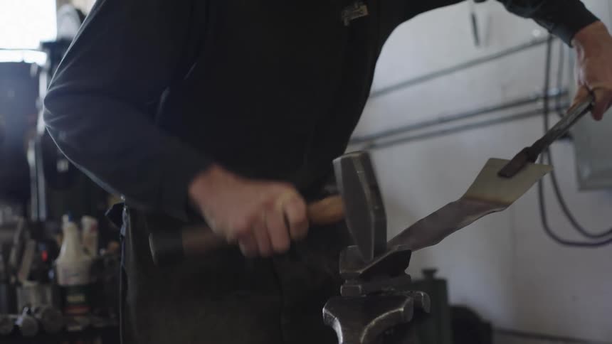 A blacksmith shaping a piece of metal with a hammer over an anvil