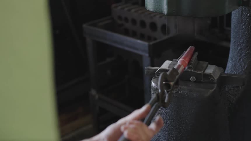 A blacksmith shapes a piece of hot metal with a pair of tongs