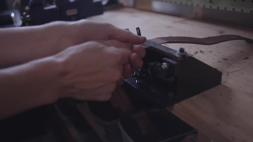 A person cuts a strip of leather using a specialized tool