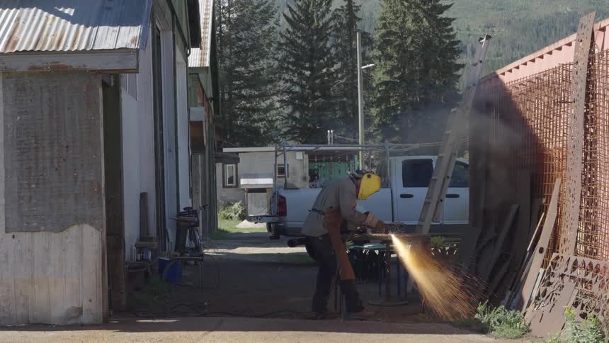 Blacksmith in protective clothing and mask cutting metal on a table