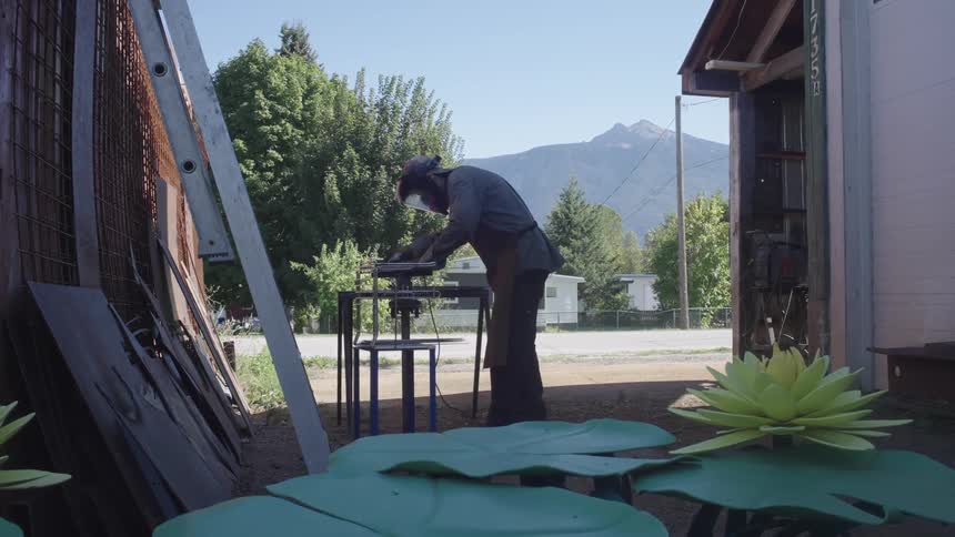A worker uses a power tool to finish a small metal structure outside a workshop