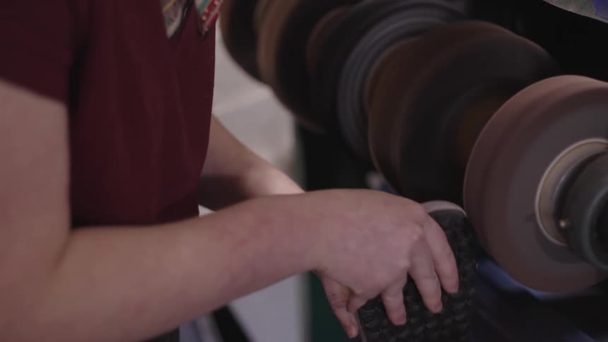 The worker carefully guides the shoe against the spinning buffing wheel creating a smooth and shiny finish