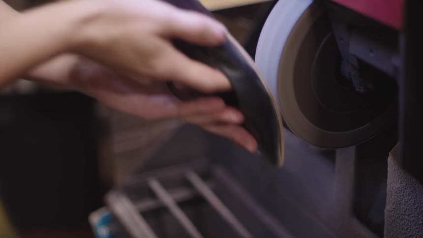 A shoemaker is using a grinder on a shoe
