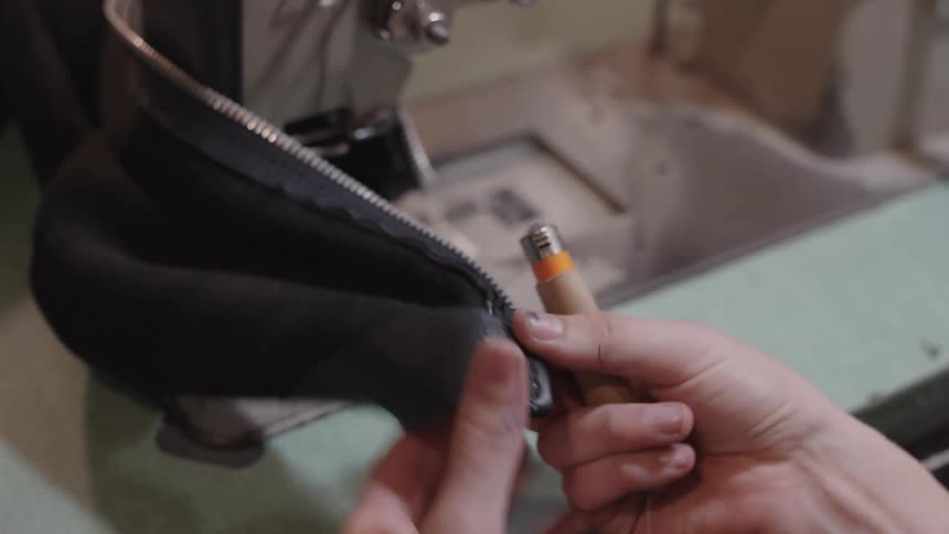 A seamstress trims excess thread with scissors and a lighter