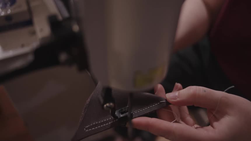 A person is using a heavy duty sewing machine to sew a brown leather piece