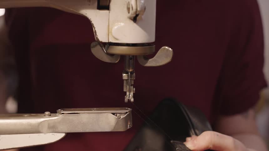 Hands of a person operating a sewing machine on a small leather bag