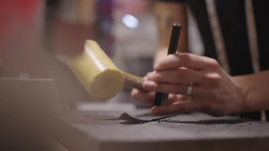 Hands of a person with a wooden hammer making holes in a metal sheet
