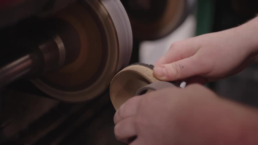 A craftsman shapes the sole of a shoe using a grinding wheel