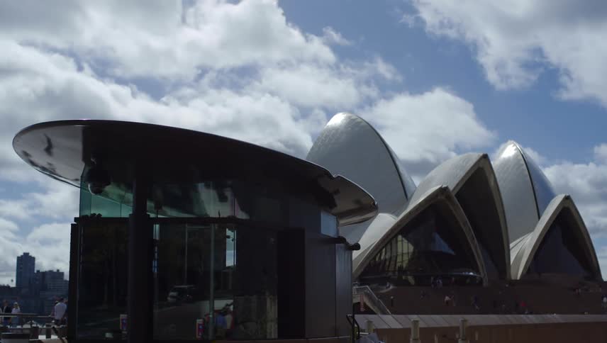 People and vehicles drive around a famous opera house and other big city structures