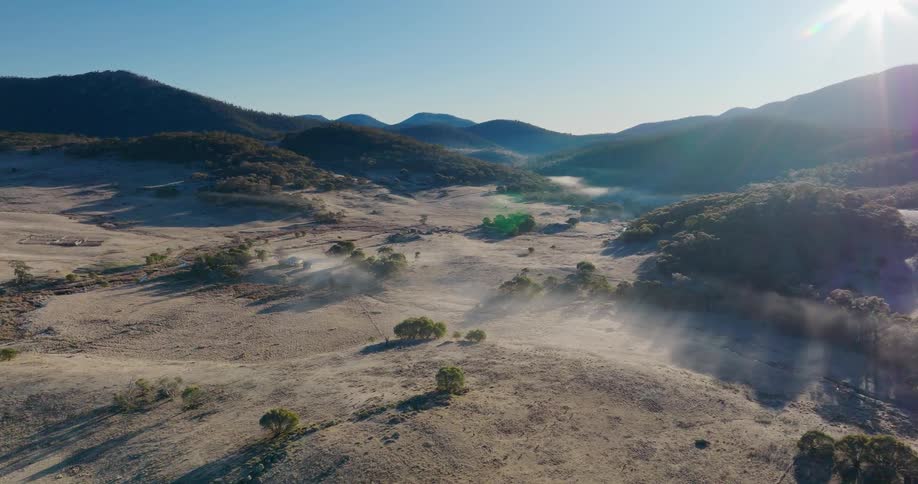 A vast dry landscape with rolling hills and distant mountains under a clear blue sky