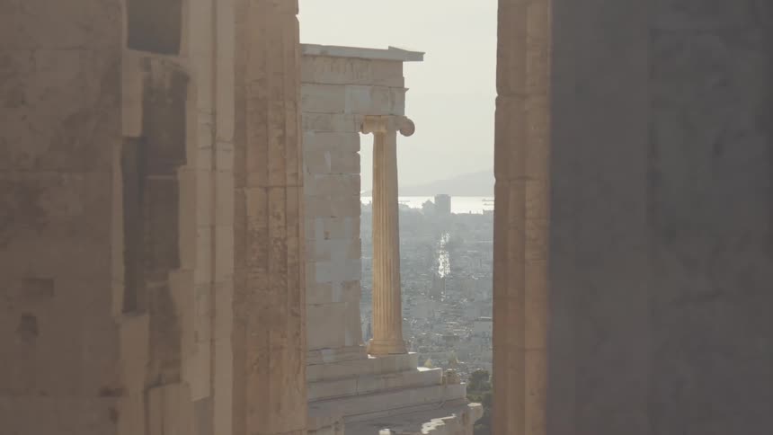 Ancient columns seen through two blurred columns with a cityscape and a body of water in the background