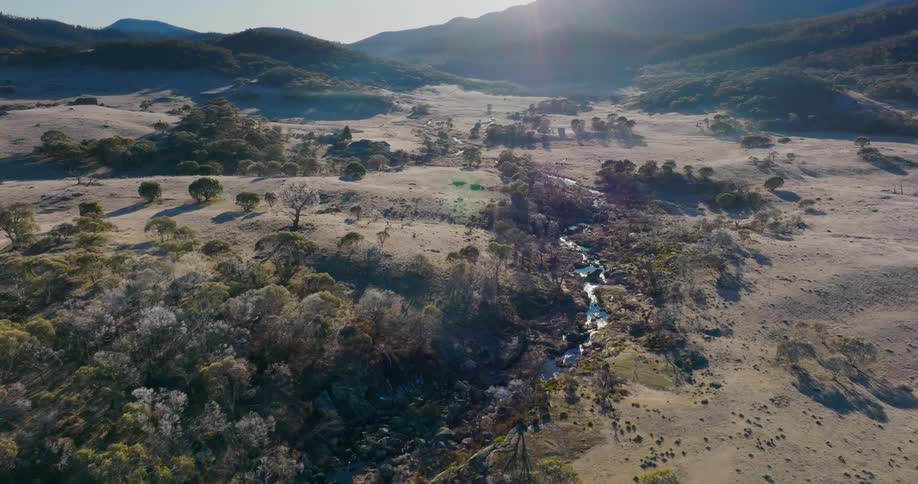 The sun casts long shadows across the rolling hills where a winding river cuts through the dry golden landscape